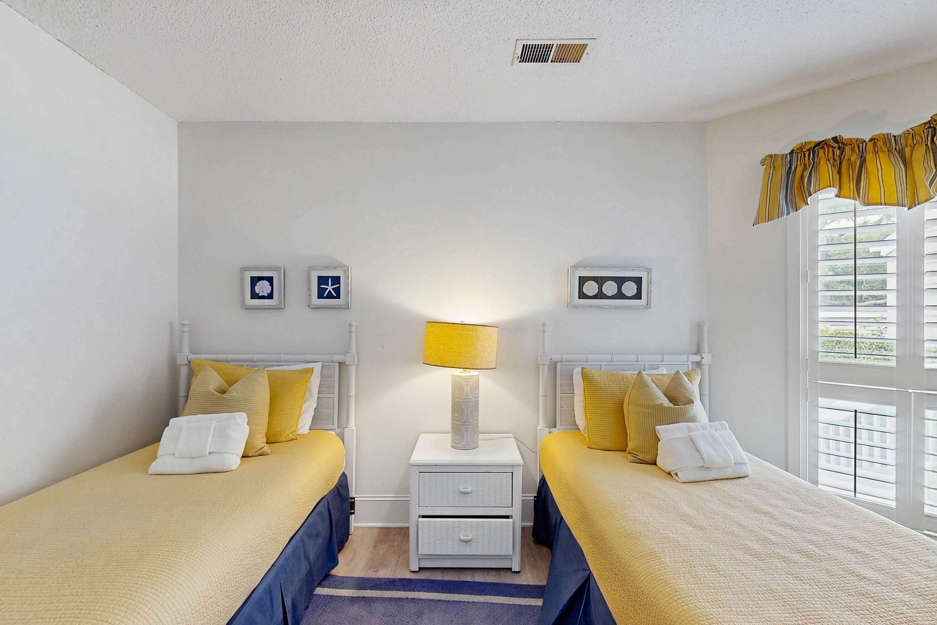 Hotellihuone, jossa on kaksi sänkyä, yöpöytä lampun kanssa ja ikkuna, jossa on sälekaihtimet.