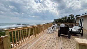 Een houten terras met tuinmeubilair, uitzicht op de oceaan en een gebouw met een deur.