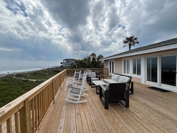 A deck with outdoor furniture overlooking the ocean, a house with large windows, and a view of the beach. - Recently updatedDog-friendly oceanfront home, lots of deck space & game room (Folly Beach)