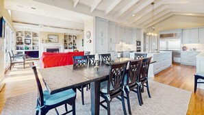 A spacious kitchen with white cabinets, a wooden dining table, and a red sofa in the living area. - Gorgeous home with panoramic ocean views, private pool, & hot tub (Seabrook Island)