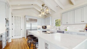 A spacious kitchen with a large island, stainless steel appliances, and a modern chandelier. - Gorgeous home with panoramic ocean views, private pool, & hot tub (Seabrook Island)
