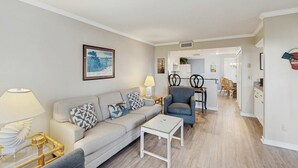 Una sala de estar moderna con un sofá, un sillón y una mesa de centro. En el fondo se ve una zona de comedor con una mesa y sillas.