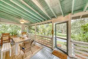 Une terrasse couverte avec une table et des chaises, un plafond en bois et une vue sur la verdure environnante.