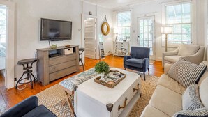 Un salon spacieux doté d’un grand téléviseur à écran plat, d’un ventilateur de plafond et d’un coin salon confortable avec un canapé et des fauteuils.