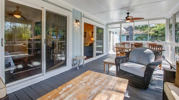 A covered outdoor area with a wooden table, wicker furniture, and sliding glass doors leading to a room. - Palm-surrounded abode with screened-in balcony, chef's kitchen, smart TVs, & W/D (Isle of Palms)
