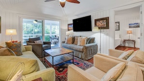 A spacious living room with a ceiling fan, a large flat-screen TV mounted on the wall, and a sliding glass door leading to an outdoor area. - Palm-surrounded abode with screened-in balcony, chef's kitchen, smart TVs, & W/D (Isle of Palms)