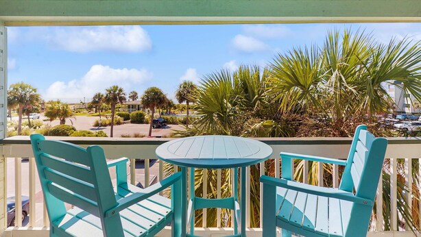 Un balcon avec des chaises turquoise et une petite table, donnant sur un parking et des palmiers.