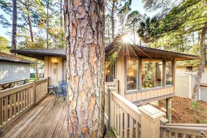 A cabin with a deck, a large tree, and a view of the surrounding forest. - Beautiful Home in the Woods with Updated Amenities and Shared Pool (Kiawah Island)