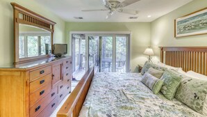 Ein Schlafzimmer mit einem großen Bett, einer Holzkommode, einem Deckenventilator und Blick durch eine Glastür auf eine Terrassenanlage.