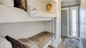 A bunk bed with white and brown bedding, a hat on the wall, and a door leading to a hallway. - Updated Oceanfront Condo w/ Balcony, Pool & Beach Access (Isle of Palms)