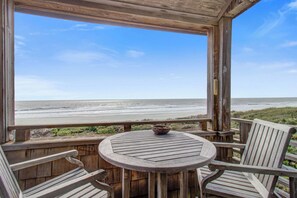 Eine Holzterrasse mit einem runden Tisch und zwei Stühlen, mit Blick auf einen Strand.