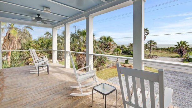 A covered outdoor area with a wooden deck, white rocking chairs, and a glass table. - Beautiful ocean view home w/ free WiFi is just across the street from the beach (Folly Beach)