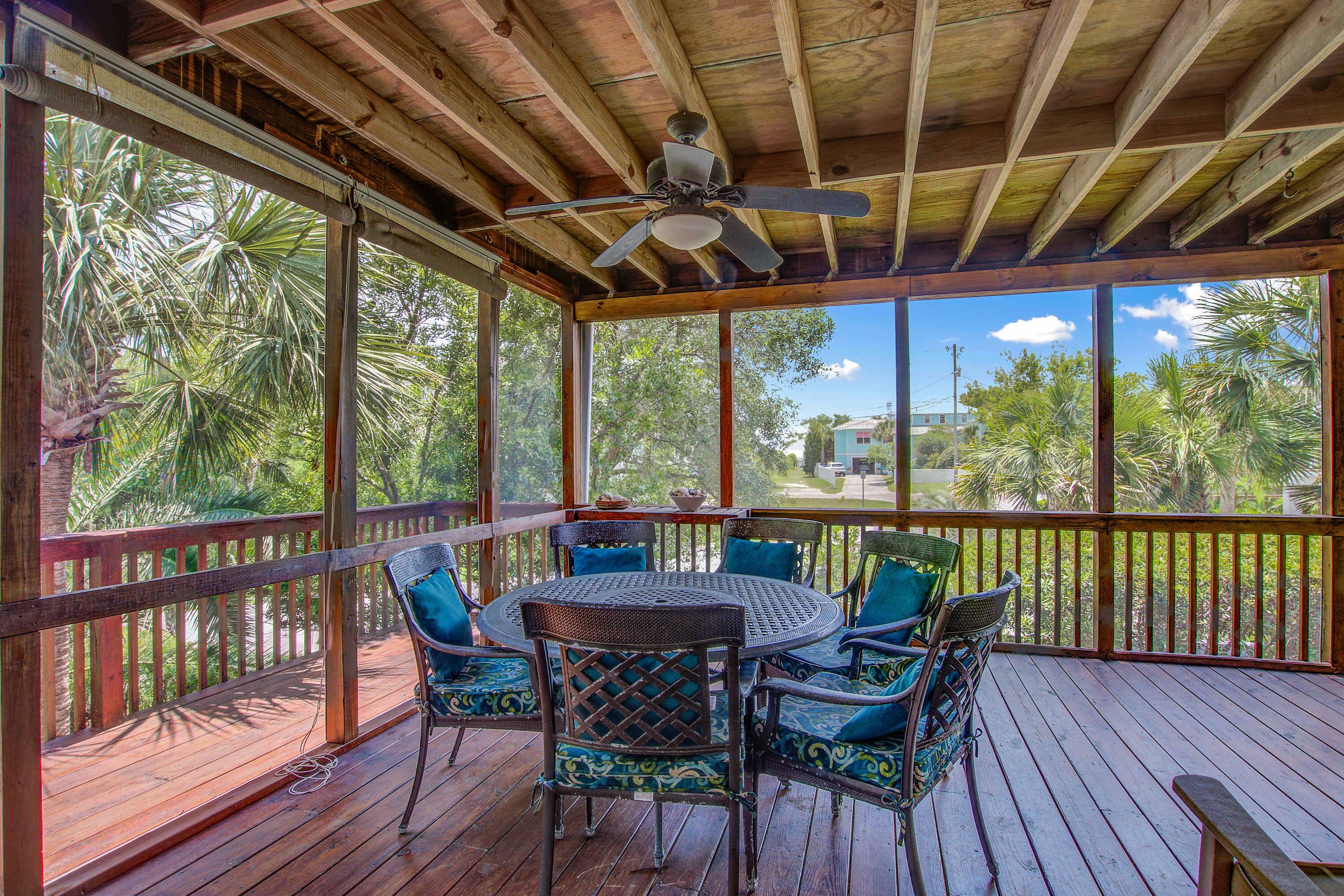 A covered outdoor area with a wooden deck, a round table with chairs, and a ceiling fan.