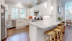 Une cuisine moderne avec des meubles blancs, un grand îlot central doté de tabourets et une vue sur l’extérieur grâce à de grandes fenêtres.