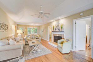 A living room with a fireplace, a ceiling fan, and a view of the outdoors.