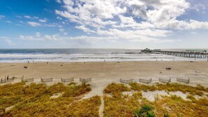 Une plage avec une jetée en bois qui s’avance dans l’océan, une plage de sable et des dunes herbeuses.