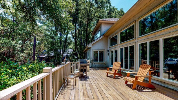 A wooden deck with outdoor seating and a grill, surrounded by trees.