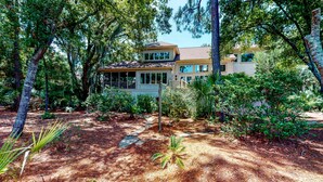A two-story house surrounded by dense trees and a well-maintained garden.