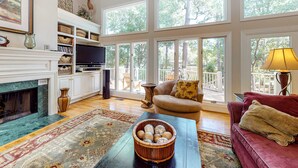 A spacious living room with a fireplace, large windows, a television, and a comfortable seating area.
