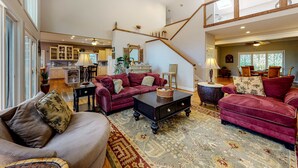 A spacious living area with a high ceiling, a staircase, and a kitchen in the background.