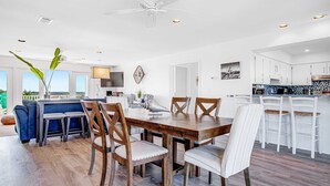 Un vaste espace dédié à la salle à manger, avec une table et des chaises en bois, un ventilateur de plafond et une vue sur l’extérieur.