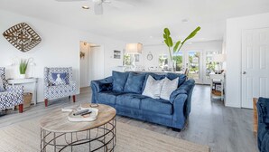 Un salon spacieux avec un canapé bleu, des fauteuils à motifs, une table basse ronde et un ventilateur de plafond.