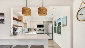 Une cuisine moderne dotée d’un îlot central, d’appareils électroménagers en acier inoxydable et de luminaires suspendus en osier.