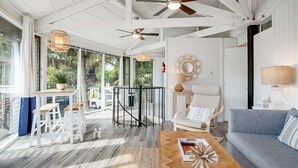 A spacious living area with a wooden coffee table, a grey sofa, and a white chair. There is a large window providing a view of the outdoors. - Lakefront home with lagoon view, deck & AC - close to beach, golf, & pools (Seabrook Island)