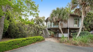 A modern house with a glass elevator, surrounded by lush greenery and trees. - Lakefront home with lagoon view, deck & AC - close to beach, golf, & pools (Seabrook Island)