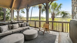 En overdækket udendørs siddeplads med sofa, skammel og fletstol med udsigt over en golfbane.