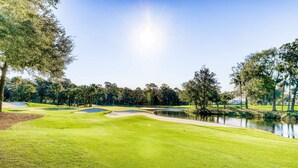 Un campo de golf con un estanque, árboles y cielo despejado.