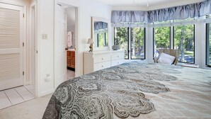 Un dormitorio con una cama grande, un ventilador de techo, una ventana con vistas al exterior y una puerta que da a otra habitación.