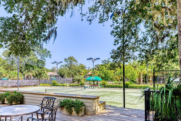 An outdoor patio area with a tennis court, seating, and greenery.