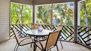 Un espacio de comedor al aire libre cubierto con una mesa redonda y sillas, ventanas amplias con vistas a palmeras y un edificio.