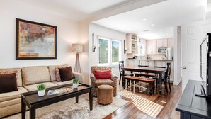 A living room with a sofa, coffee table, and ottoman, a dining area with a table and chairs, and a kitchen with cabinets and appliances. - Townhouse-style villa with screened porch & pool access - short walk to beach (Isle of Palms)