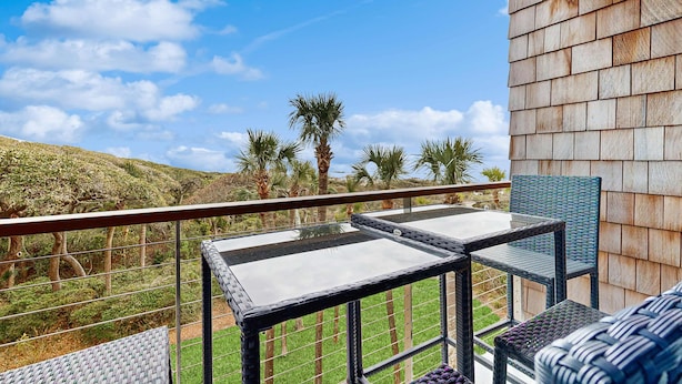 Un balcone con tavolo e sedie in vetro, affacciato su un paesaggio collinare con palme.