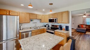 Una cocina moderna con encimeras de granito, electrodomésticos de acero inoxidable, armarios de madera e iluminación colgante.