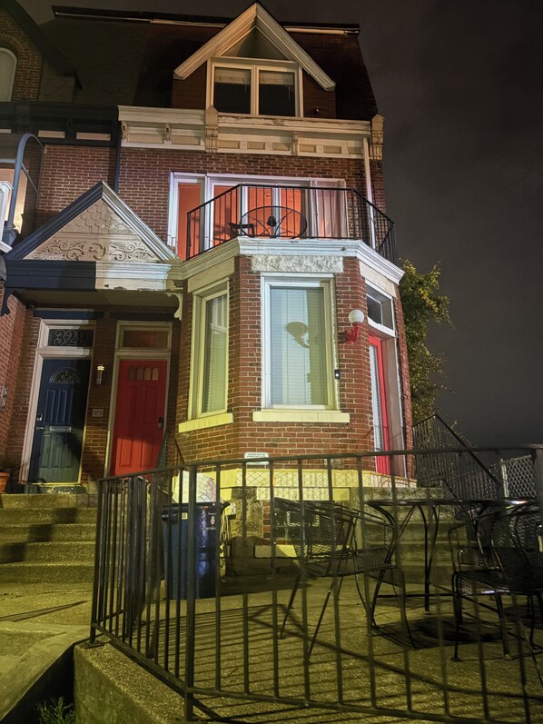A two-story house with a red door, a balcony with a black railing, and a window with a white frame. - M&T Grandview (Pittsburgh)