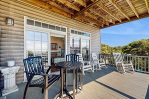 A wooden deck with outdoor furniture, a covered area with a wooden ceiling, and a view of a house with large windows. - First-floor villa w/partial ocean views, covered porch -one block from the beach (Folly Beach)