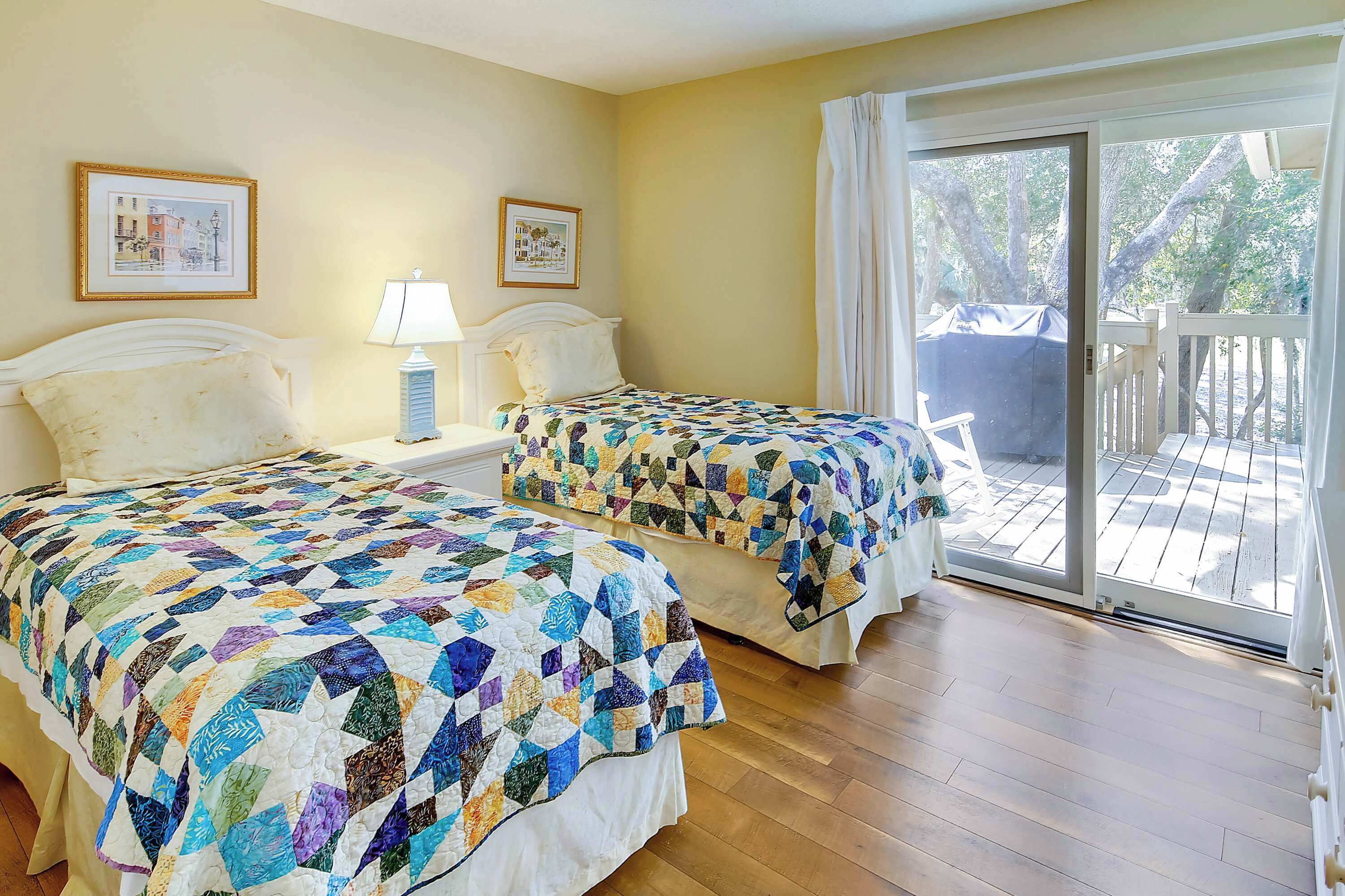 A room with two beds, each with a colorful quilt, a nightstand with a lamp, and a window with a view of the outdoors.