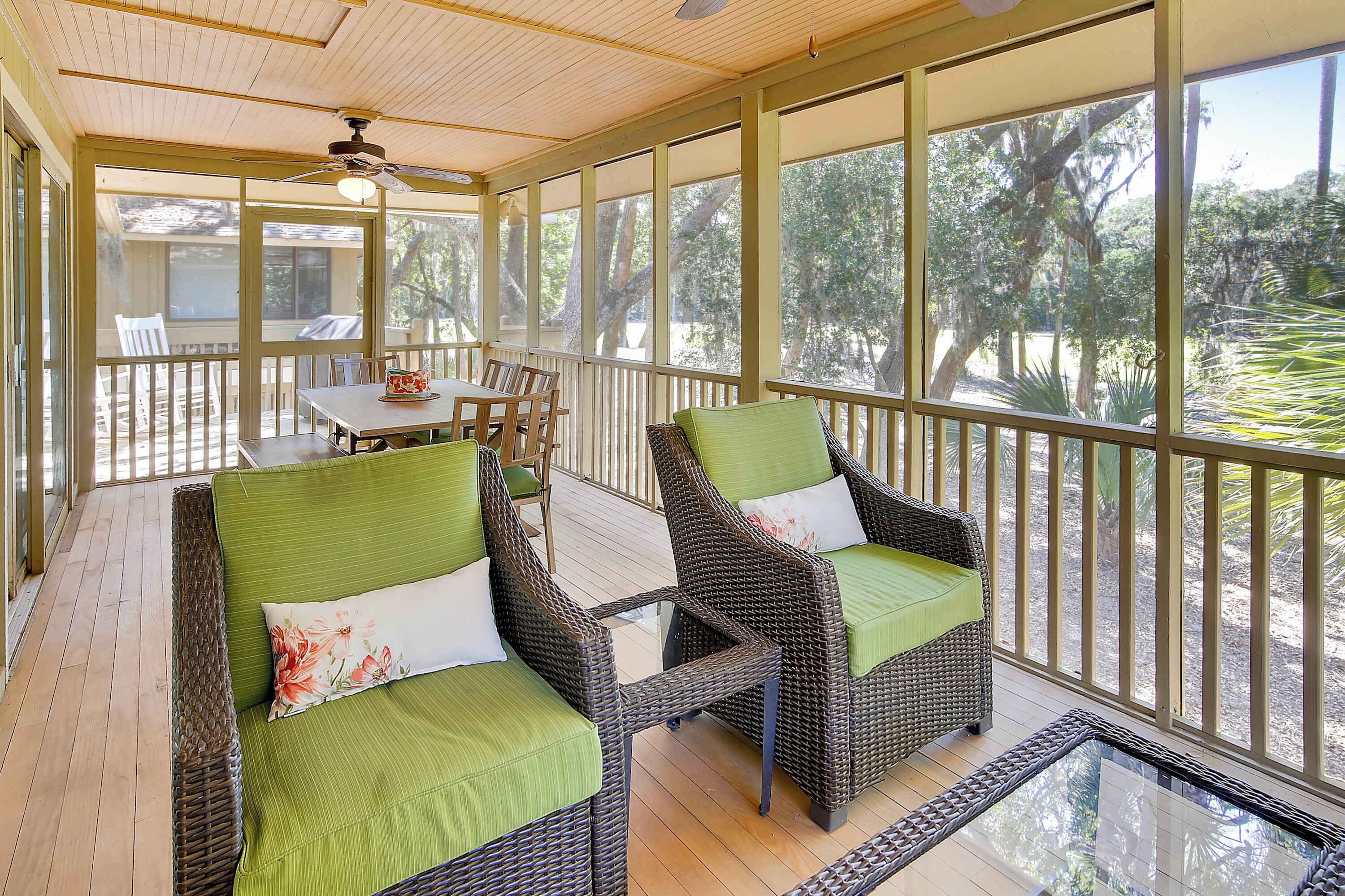 A covered porch with wicker furniture, a table, and chairs, overlooking a wooded area.