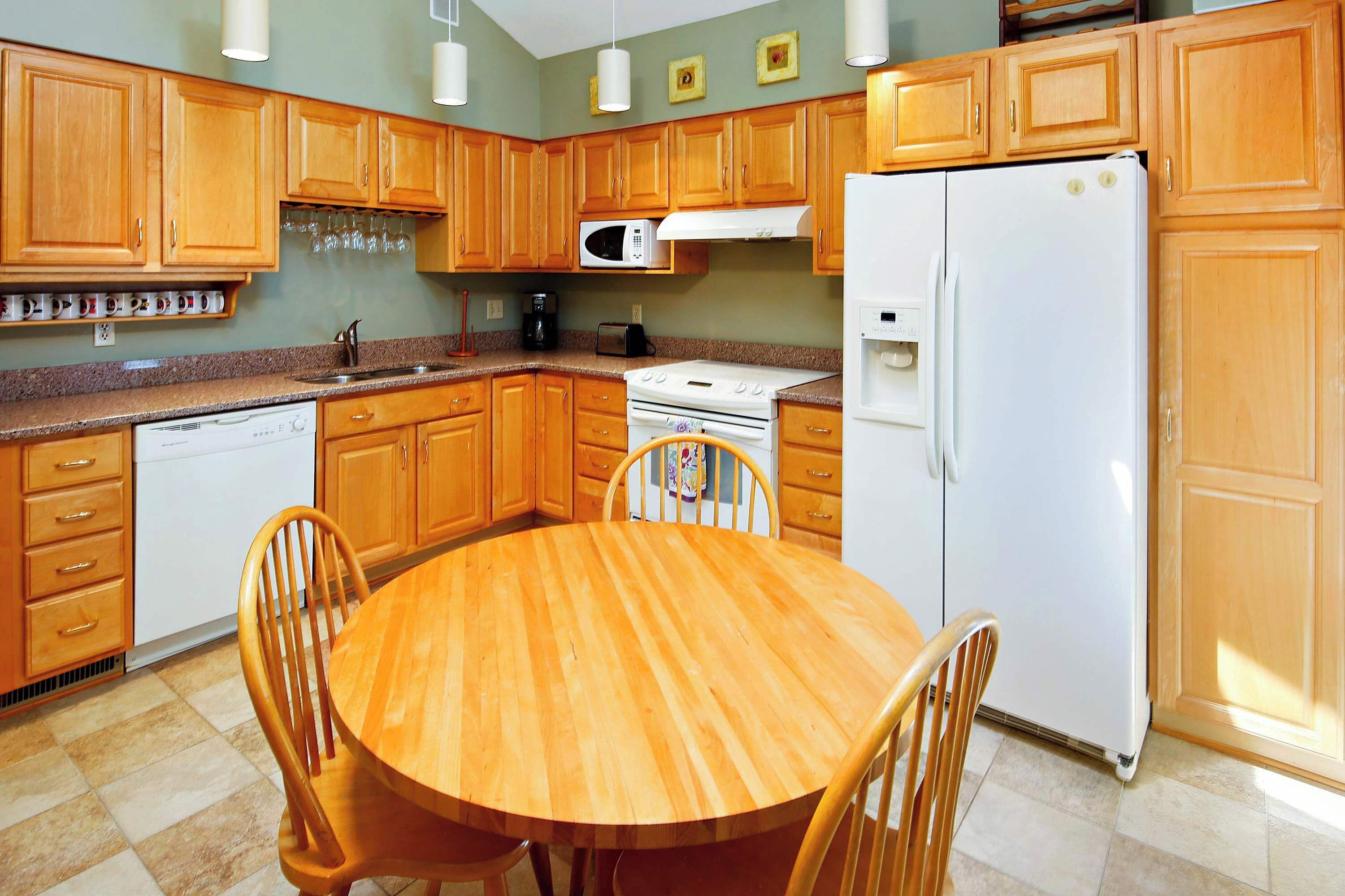 A kitchen with wooden cabinets, a white refrigerator, a microwave, a stove, and a dining table with chairs.