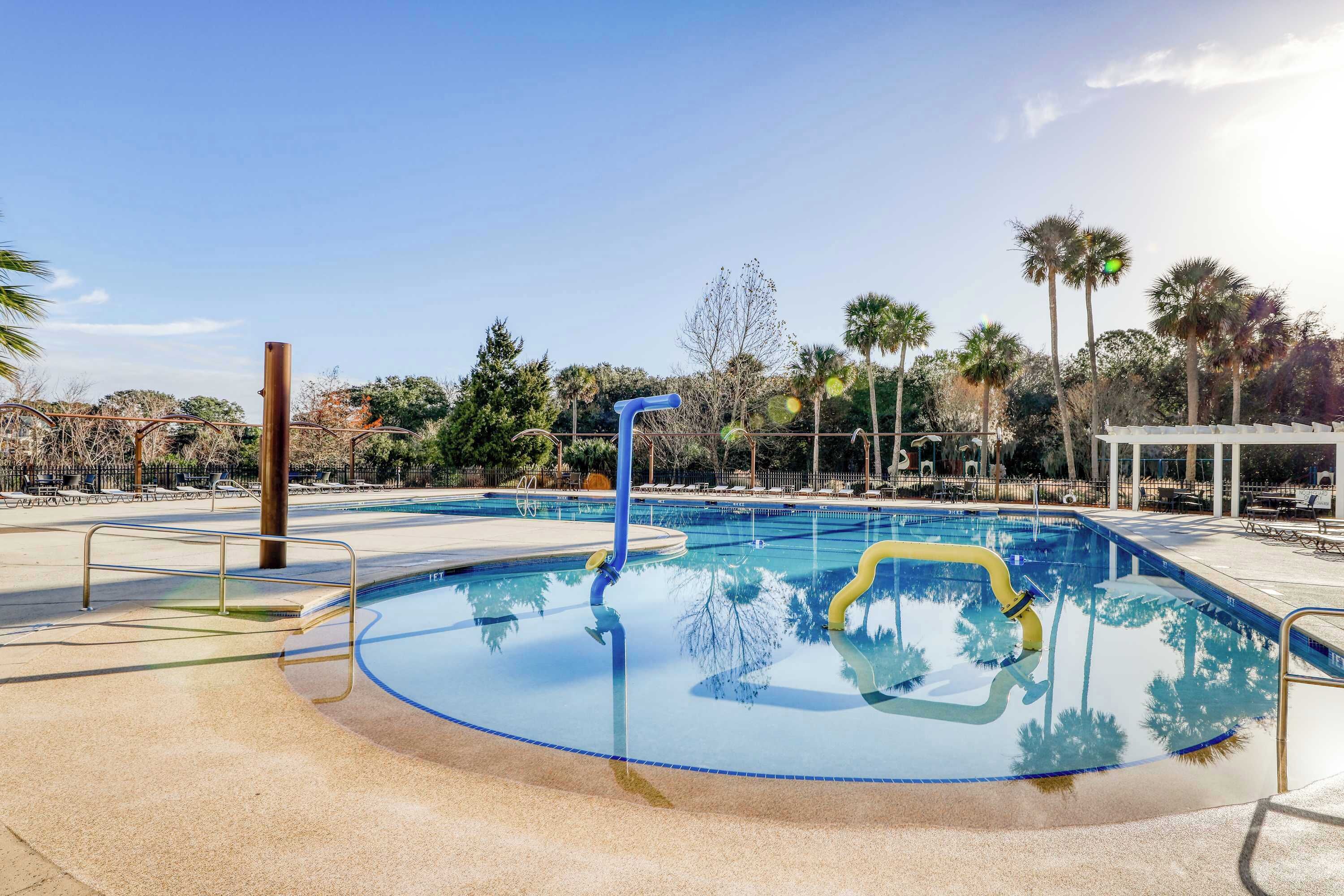 Una piscina con un tobogán de color azul y amarillo, rodeada de palmeras y una cerca blanca.