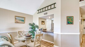 A dining area with a glass table, wooden chairs, and a plant. There is a kitchen visible in the background. - Beach villa with full kitchen, ocean/inlet views - short walk to Beach Club (Seabrook Island)