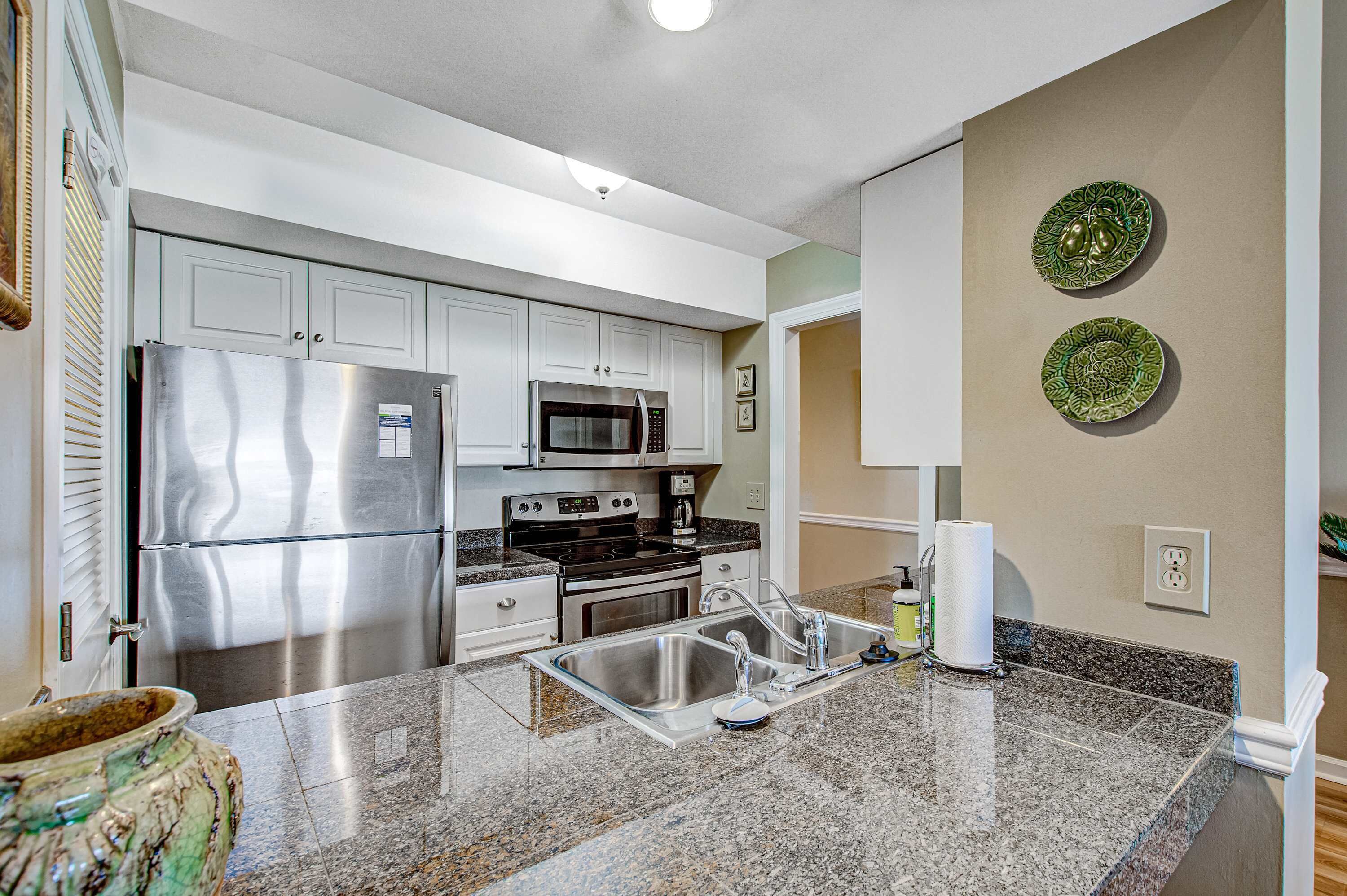 Cozinha moderna com eletrodomésticos de aço inoxidável, bancadas de granito e detalhes decorativos nas paredes.