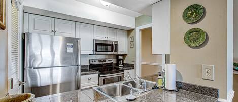 Cozinha moderna com eletrodomésticos de aço inoxidável, bancadas de granito e detalhes decorativos nas paredes.