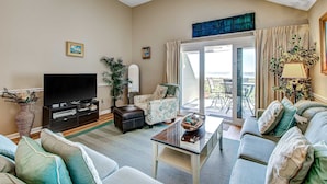 A living room with a flat-screen TV, a sofa, a coffee table, and a view of the outdoors through a sliding glass door. - Beach villa with full kitchen, ocean/inlet views - short walk to Beach Club (Seabrook Island)
