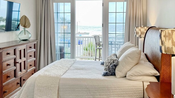 Een slaapkamer met een groot bed, een dressoir, een televisie en een balkon met uitzicht op de zee.