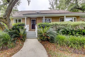 A two-story house with a front porch, a pathway leading to the door, and various plants around the property. - Beautiful home on lush lot with boardwalk to marsh, large deck, wifi, central ac (Isle of Palms)