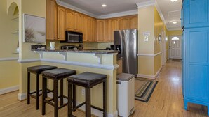 A kitchen with wooden cabinets, a stainless steel refrigerator, a microwave, and a bar area with stools.